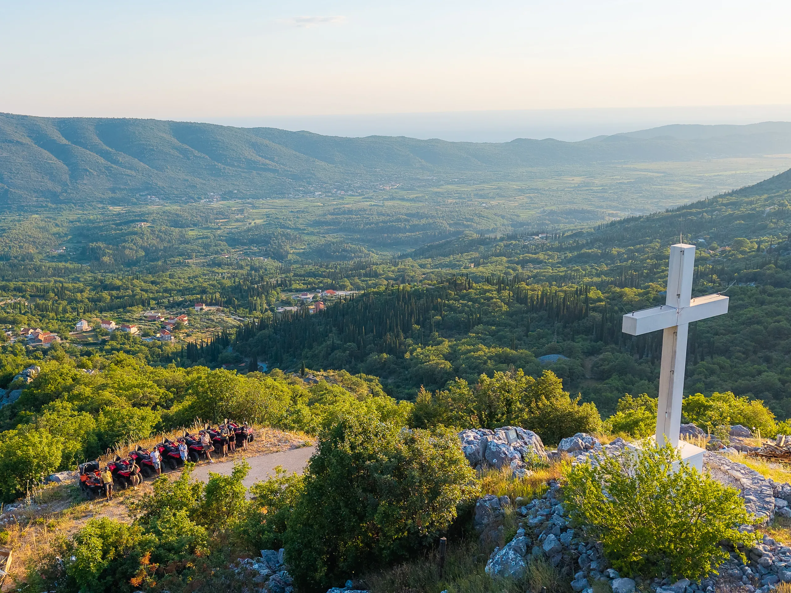 ATV quads parked beside the white cross at the St. Barbara viewpoint, the Konavle valley stretching to the sea below