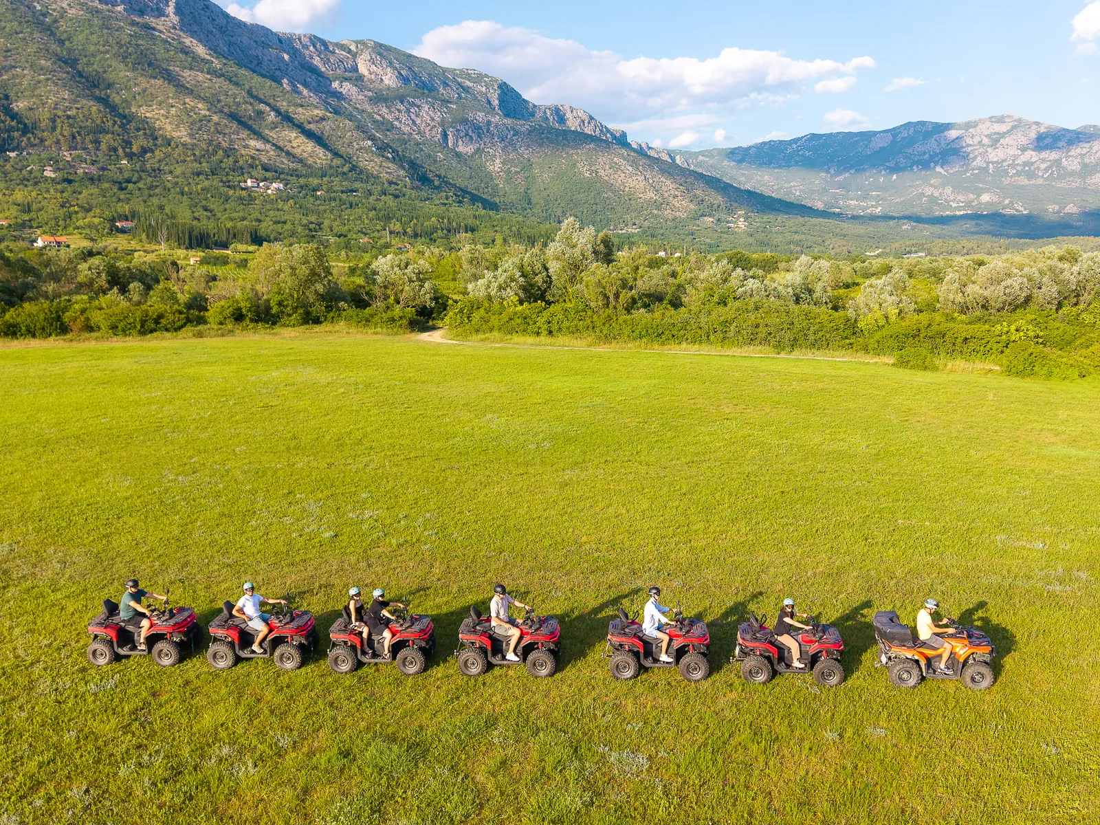 Aerial view of a line of ATV quads crossing the green Konavle field