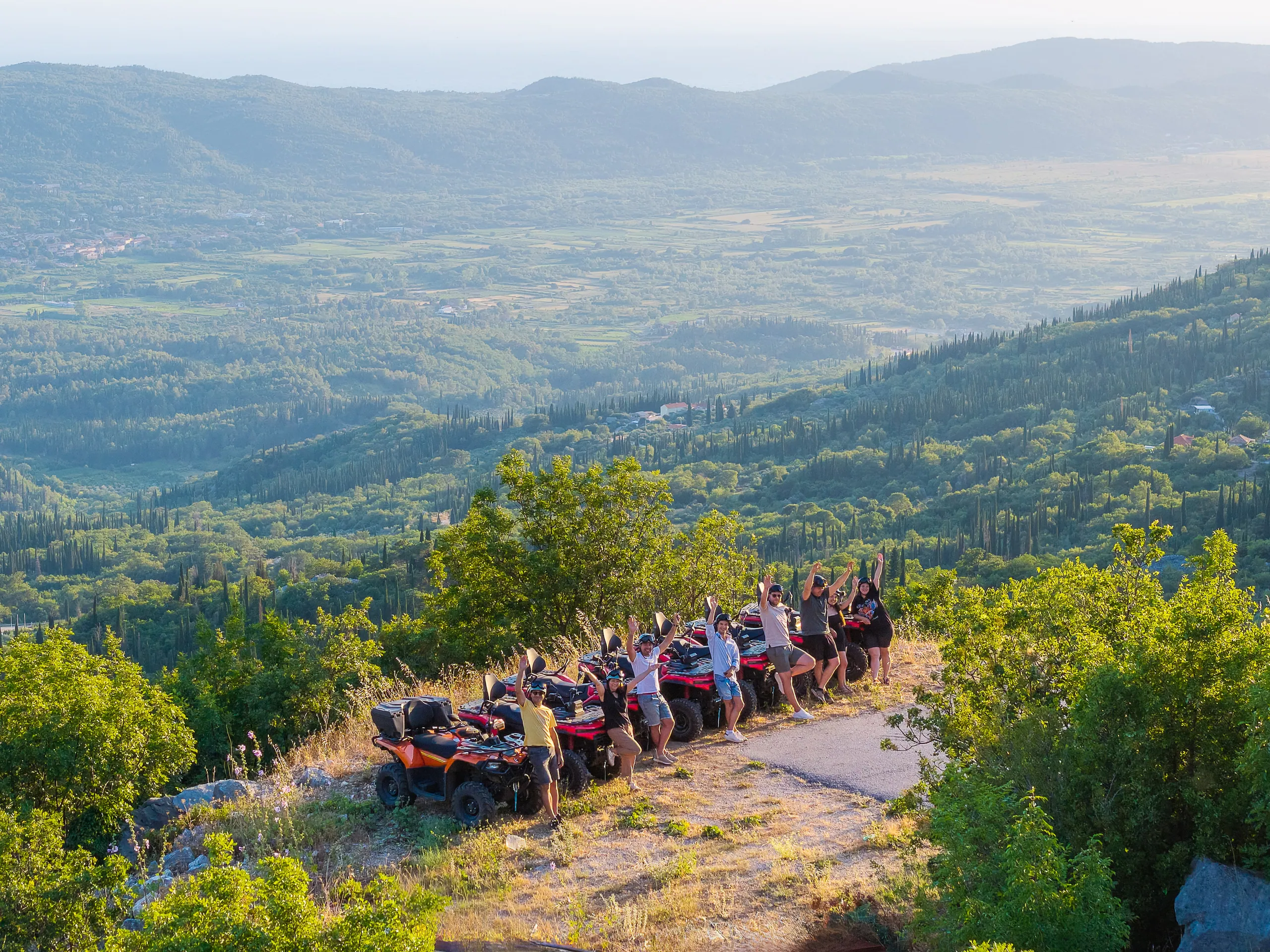 Group of riders raising their arms beside their quads at a viewpoint over the Konavle valley